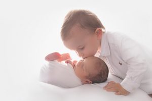 A brother is kissing his newborn baby brother during their baby photography session in Sydney.