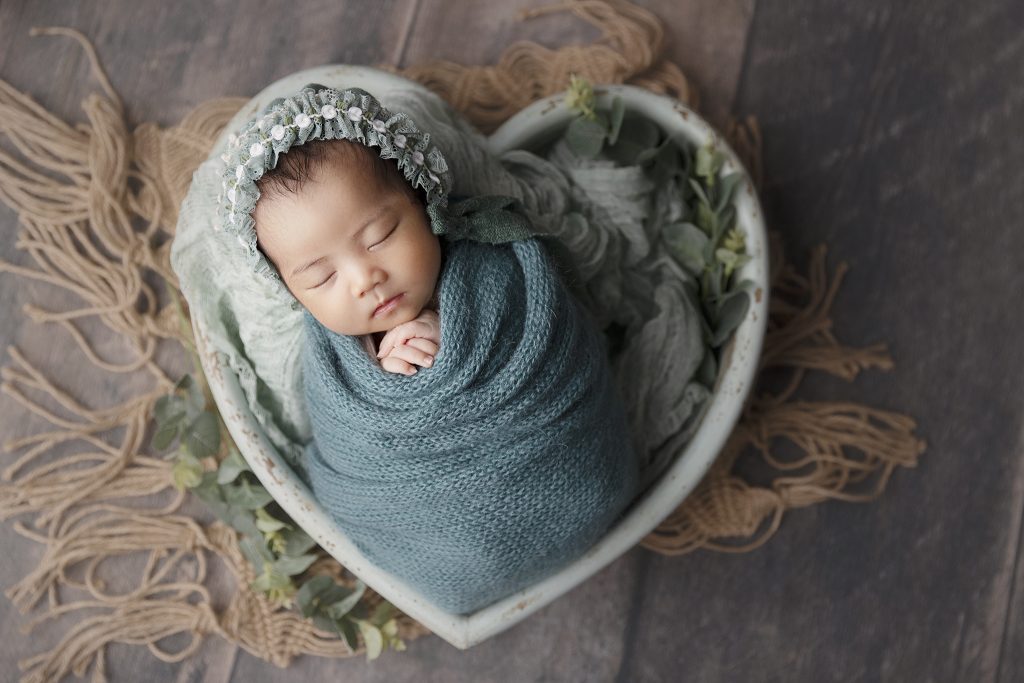 Cute baby girl posed in a wooden heart shape bowl.