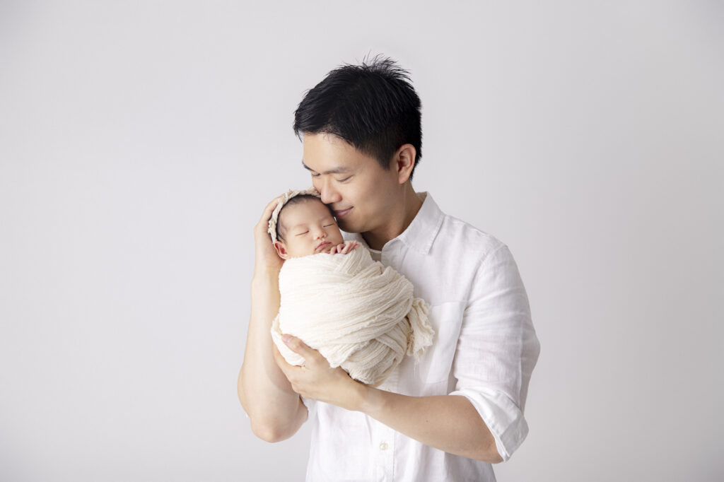 A father is holding his baby girl in his arms during her newborn photoshoot in Sydney.